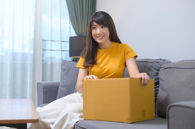 A young smiling woman opening cardboard box in living room at home