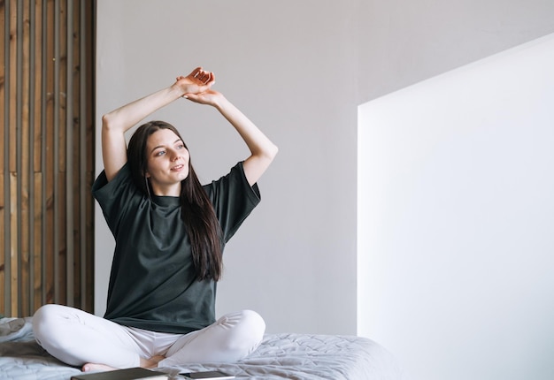 Young smiling woman teenager girl with dark long hair in jeans sitting on bed in her room