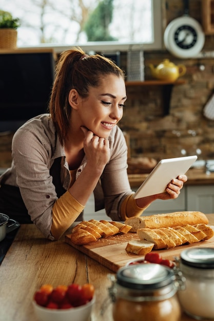 Young smiling woman using digital tablet while preparing food in the kitchen