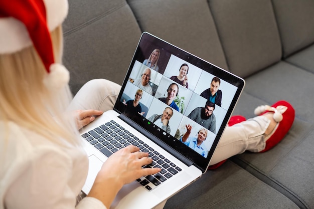 A young smiling woman wearing red Santa Claus hat making video call on social network with family and friends on Christmas day.