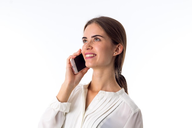 Young smiling woman in white blouse talking on her mobile phone on white background in studio