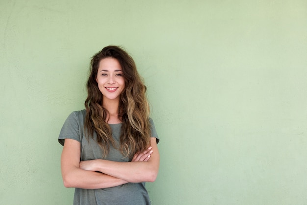 Young smiling woman with arms crossed against green background