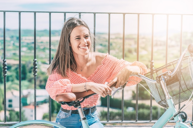 Young smiling woman with bicycle rests sitting with beautiful landscape