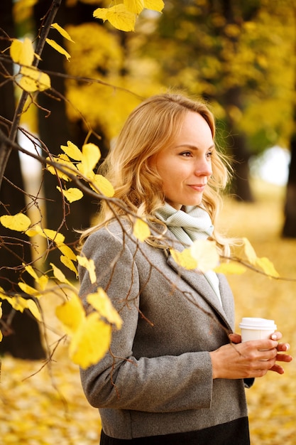 Young smiling woman with coffee outdoors in sunny autumn day closeup portrait