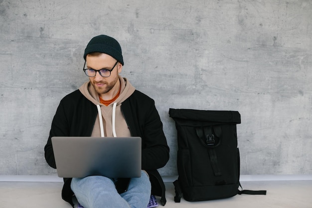 Young software developer man using laptop computer writing programming code while sitting on the floor at modern creative startup office