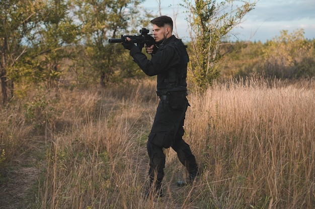 Young soldier in black uniform aiming an assault rifle