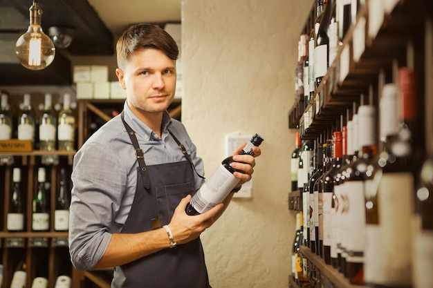 Young sommelier holding bottle of red wine in cellar