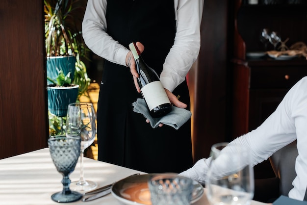 A young sommelier in a stylish uniform demonstrates and offers the client fine wine in the restaurant Customer service Table setting in a fine restaurant