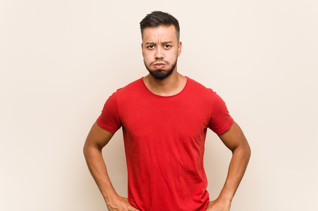 Young south asian man blows cheeks, has tired expression. Facial expression concept.