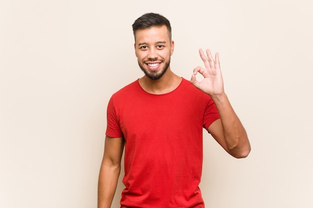 Young south-asian man cheerful and confident showing ok gesture.