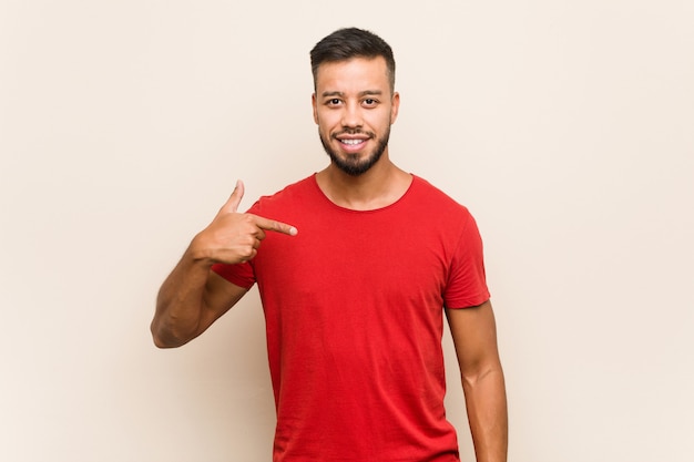 Young south-asian man person pointing by hand to a shirt copy space, proud and confident