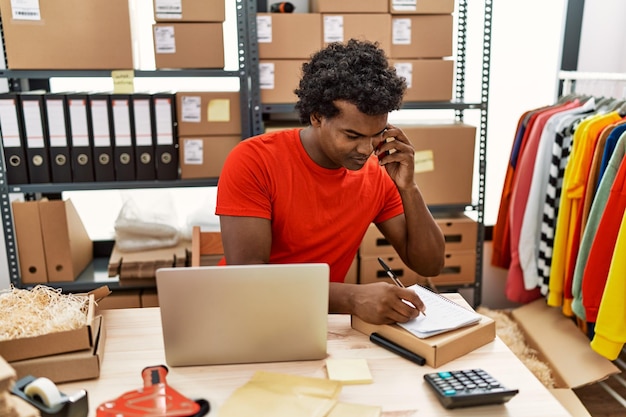 Young south east man talking on the smartphone writing order on notebook at storehouse