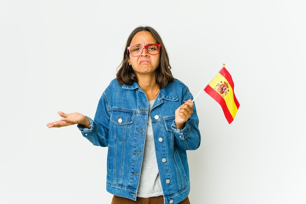 Photo young spanish woman holding a flag doubting and shrugging shoulders in questioning gesture