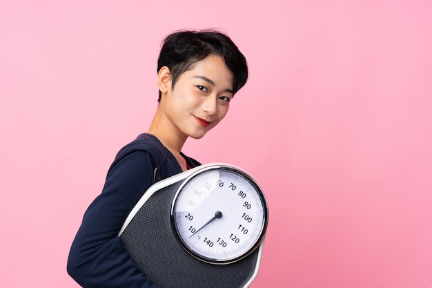 Young sport Asian woman over isolated pink wall with weighing machine