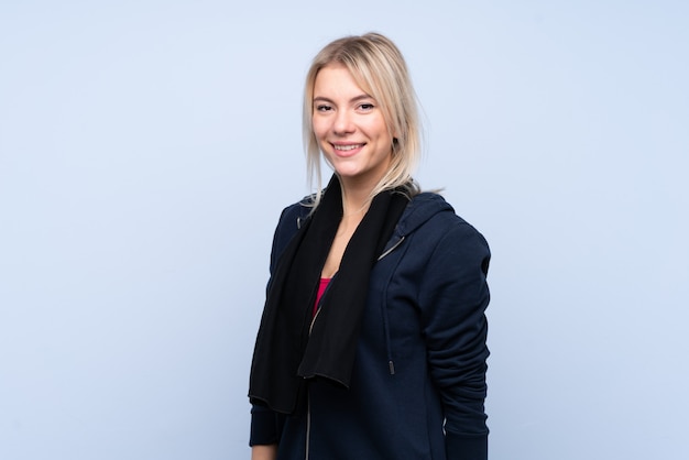 Young sport blonde woman over isolated blue wall with sport towel