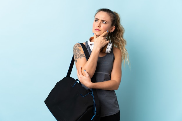 Young sport Brazilian woman with sport bag isolated on blue having doubts