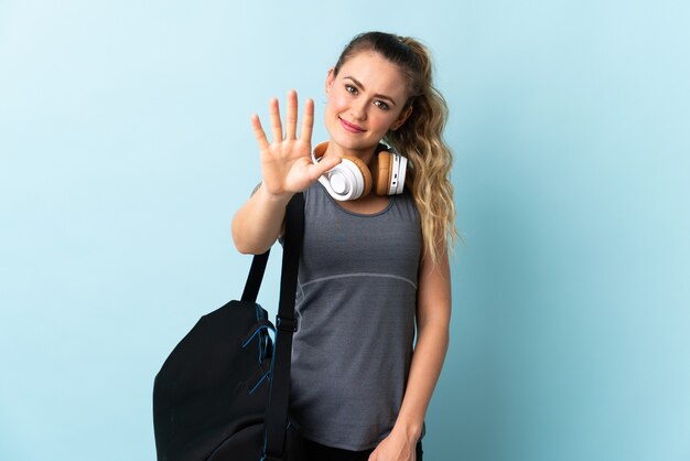 Young sport Brazilian woman with sport bag isolated on blue wall counting five with fingers