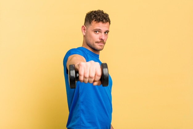 Young sport caucasian man doing weightlifting isolated on yellow background