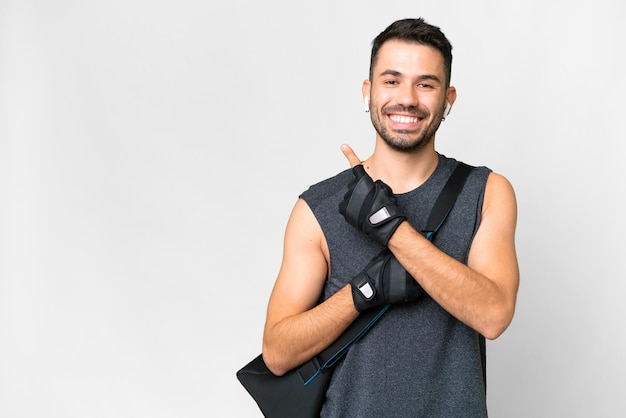 Young sport caucasian man with sport bag over over isolated white background pointing to the side to present a product