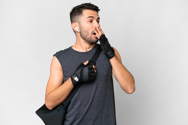 Young sport caucasian man with sport bag over over isolated white background yawning and covering wide open mouth with hand