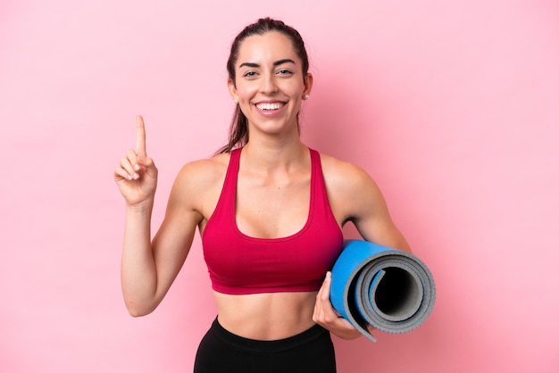 Young sport caucasian woman going to yoga classes while holding a mat isolated on pink background pointing up a great idea