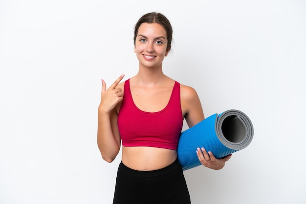 Young sport caucasian woman going to yoga classes while holding a mat isolated on white background giving a thumbs up gesture