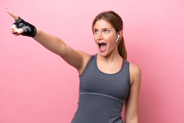 Young sport caucasian woman isolated on pink background pointing away