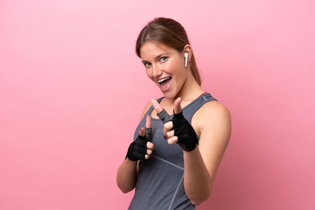 Young sport caucasian woman isolated on pink background pointing to the front and smiling