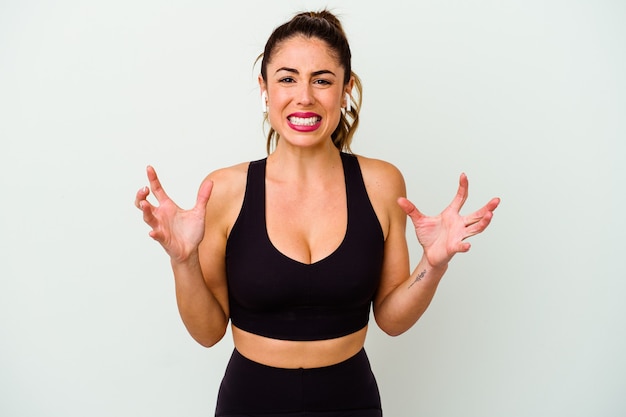 Young sport caucasian woman isolated on white background screaming with rage.