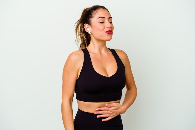 Young sport caucasian woman isolated on white touches tummy, smiles gently, eating and satisfaction concept.