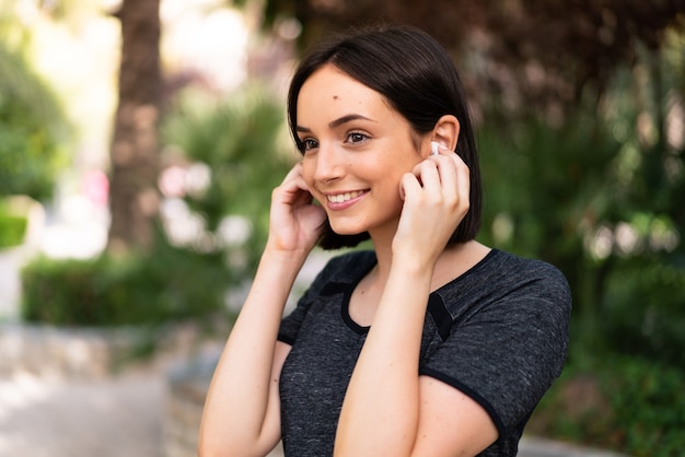 Young sport caucasian woman listening music at outdoors in a park