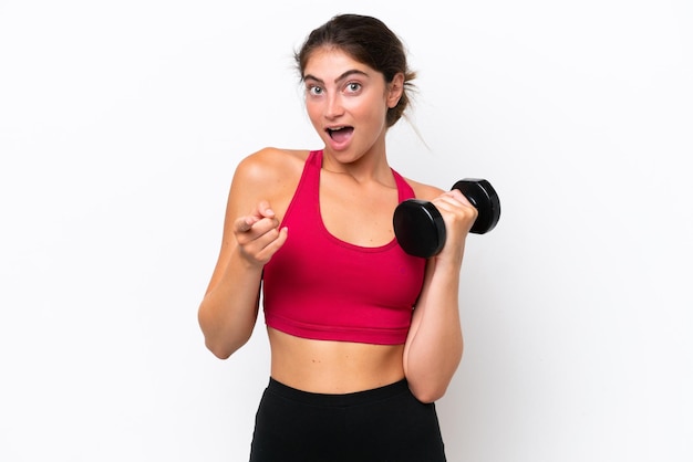 Young sport caucasian woman making weightlifting isolated on white background surprised and pointing front