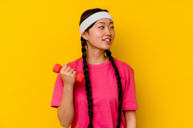 Young sport chinese woman isolated on yellow background looks aside smiling, cheerful and pleasant.