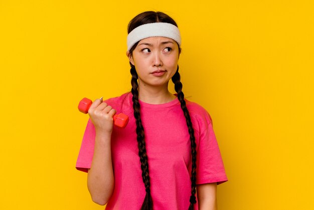 Young sport chinese woman isolated on yellow wall confused, feels doubtful and unsure