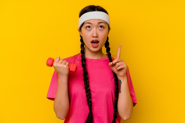 Young sport chinese woman isolated on yellow wall pointing upside with opened mouth