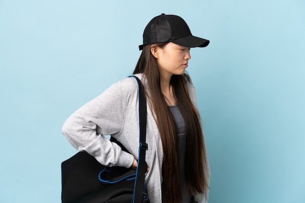 Photo young sport chinese  woman with sport bag over isolated blue suffering from backache for having made an effort