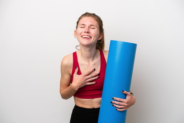 Young sport English woman going to yoga classes while holding a mat isolated on white background smiling a lot