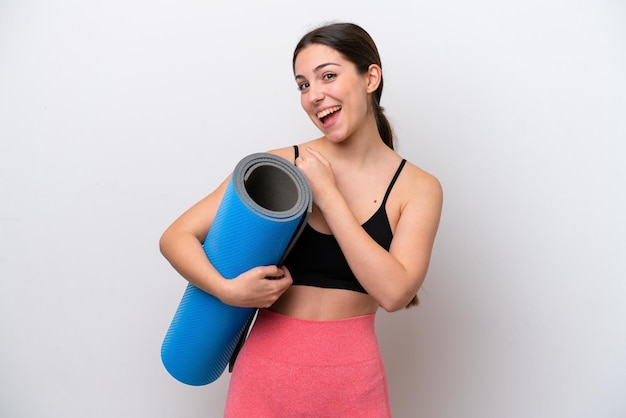 Young sport girl going to yoga classes while holding a mat isolated on white background celebrating a victory