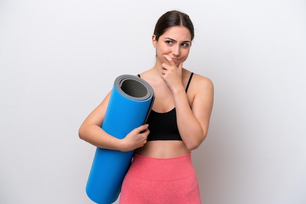 Young sport girl going to yoga classes while holding a mat isolated on white background having doubts