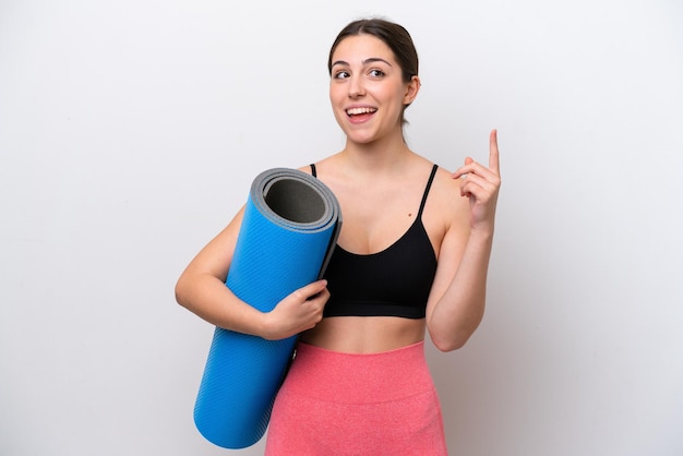 Young sport girl going to yoga classes while holding a mat isolated on white background thinking an idea pointing the finger up