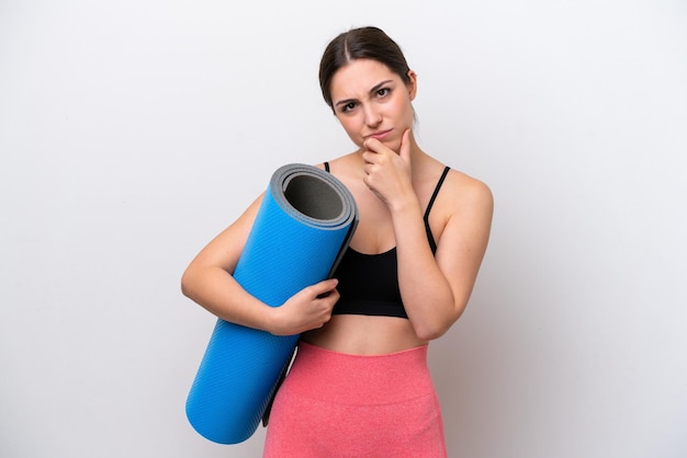 Young sport girl going to yoga classes while holding a mat isolated on white background thinking