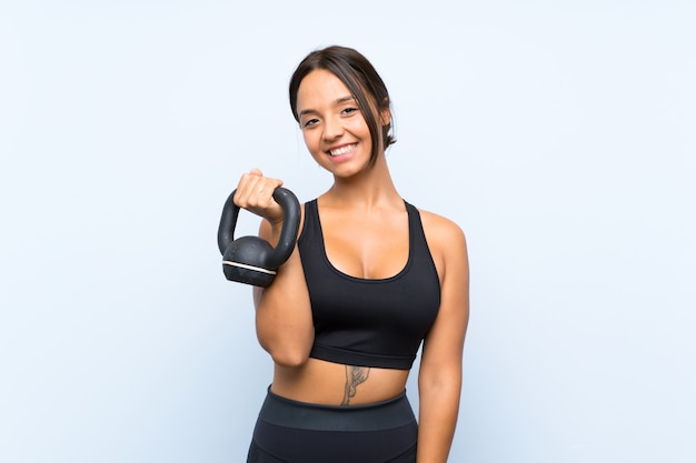 Young sport girl making weightlifting with kettlebell over isolated blue wall