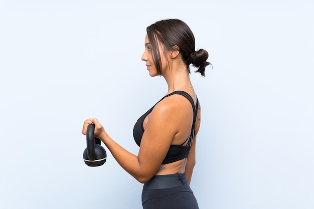 Young sport girl making weightlifting with kettlebell over isolated blue wall