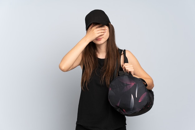 Young sport girl with sport bag isolated on grey covering eyes by hands