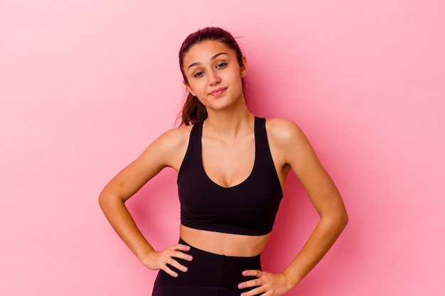 Young sport Indian woman isolated on pink background confident keeping hands on hips.