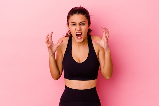 Young sport Indian woman isolated on pink screaming with rage.