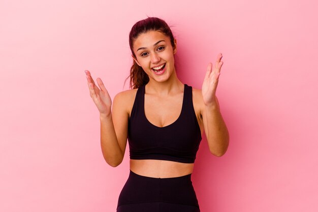 Young sport Indian woman isolated on pink wall receiving a pleasant surprise, excited and raising hands.