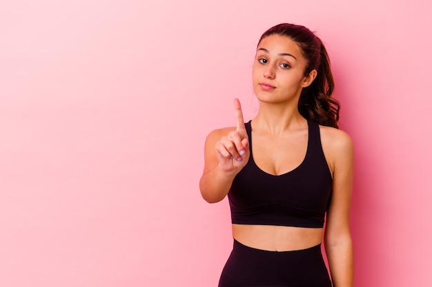 Young sport Indian woman isolated on pink wall showing number one with finger.