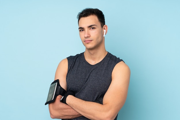 Young sport man over isolated on blue wall with arms crossed