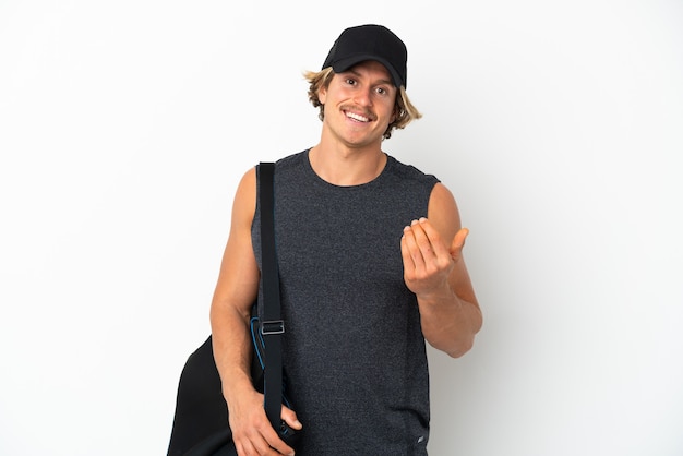 Young sport man with sport bag isolated on white wall inviting to come with hand. Happy that you came